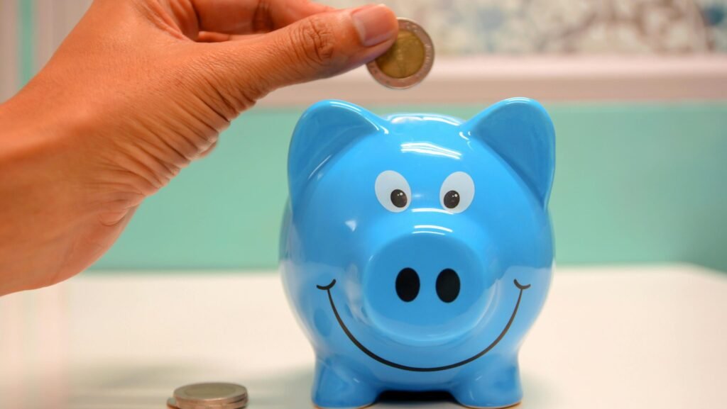 Hand inserting a coin into a blue piggy bank for savings and money management.