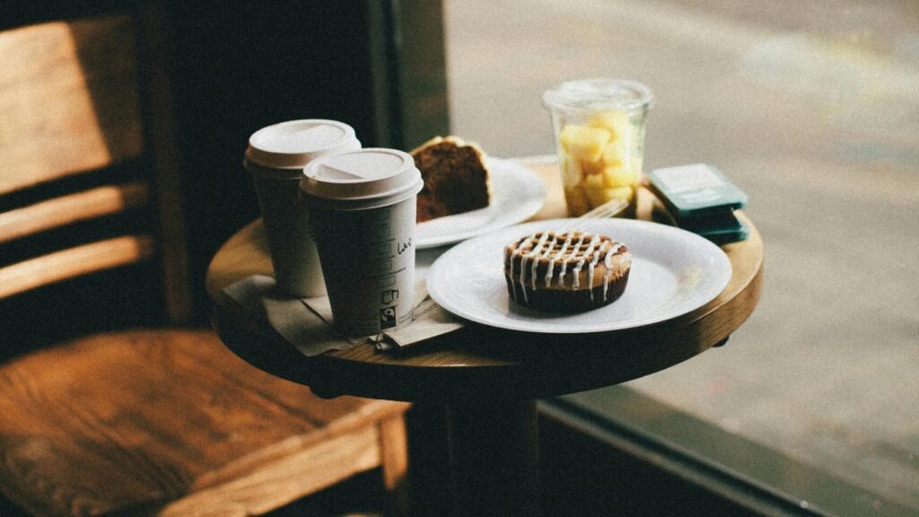 Warm lighting in a modern café with coffee, pastries, and wooden furniture by the window.