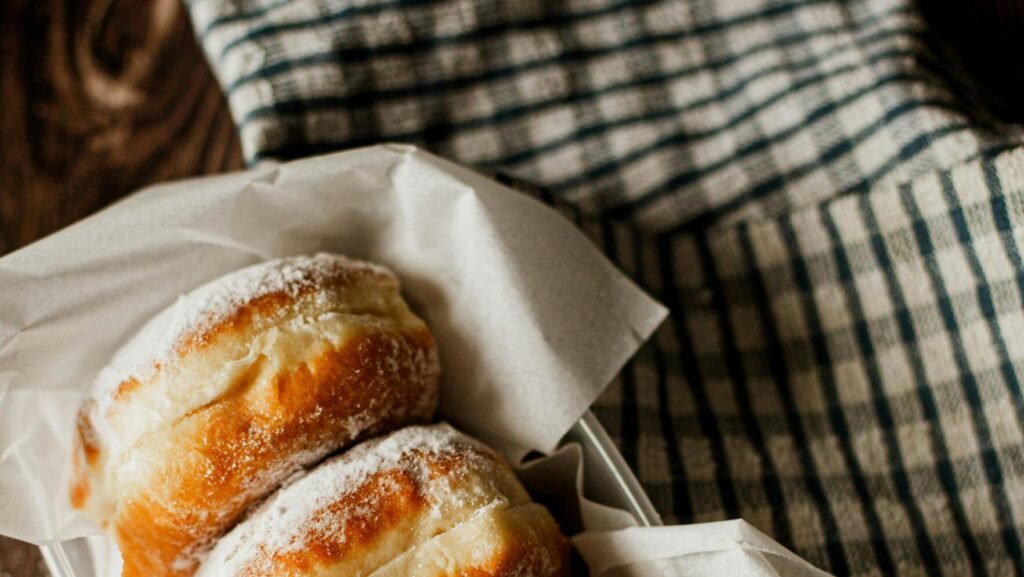 Three donuts with powdered sugar paired with a cup of black coffee, captured in warm natural light.