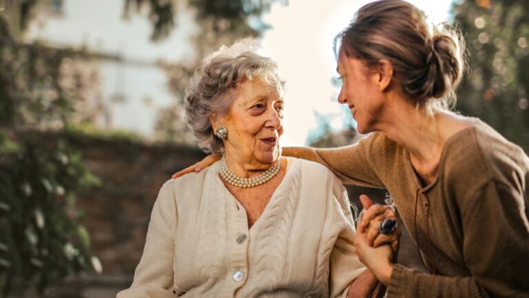 Elderly woman and adult daughter share a joyful, affectionate moment in a sunny garden.
