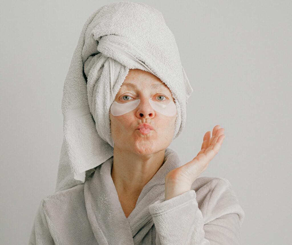 Woman with a towel on her head and eye masks, blowing a kiss in a robe.
