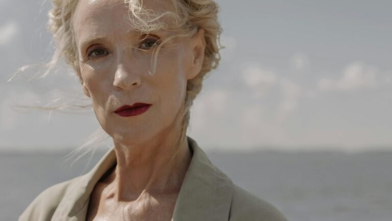 Elegant senior woman in a trench coat at the beach during sunset.