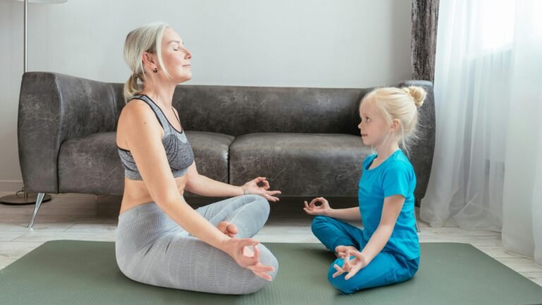 Grandmother and granddaughter practicing yoga meditation at home on a yoga mat in the living room.