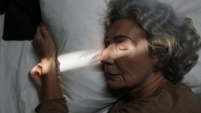 Serene image of elderly woman resting peacefully on pillow with sunlight grazing her face.
