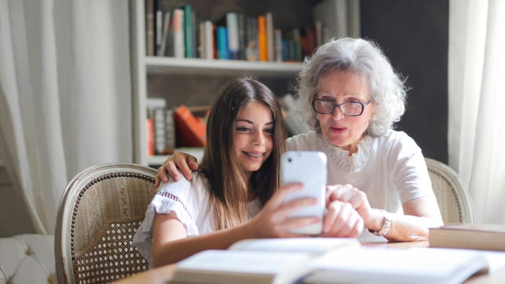 A grandmother and granddaughter bonding over a smartphone at home, showcasing generational connection.