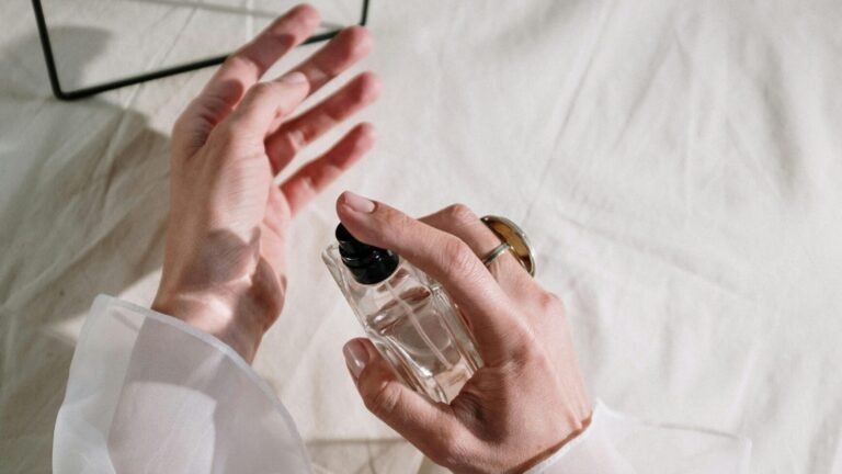 Hands in elegant sheer fabric holding perfume bottle near mirror, creating a graceful reflection.