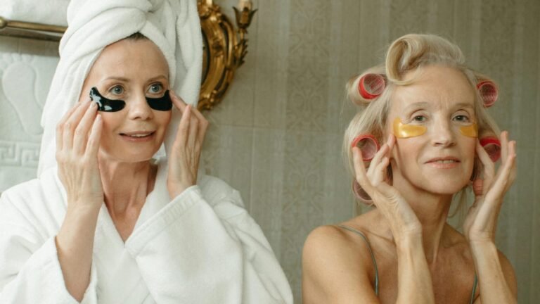 Two senior women enjoying a skincare routine with eye patches and hair rollers.