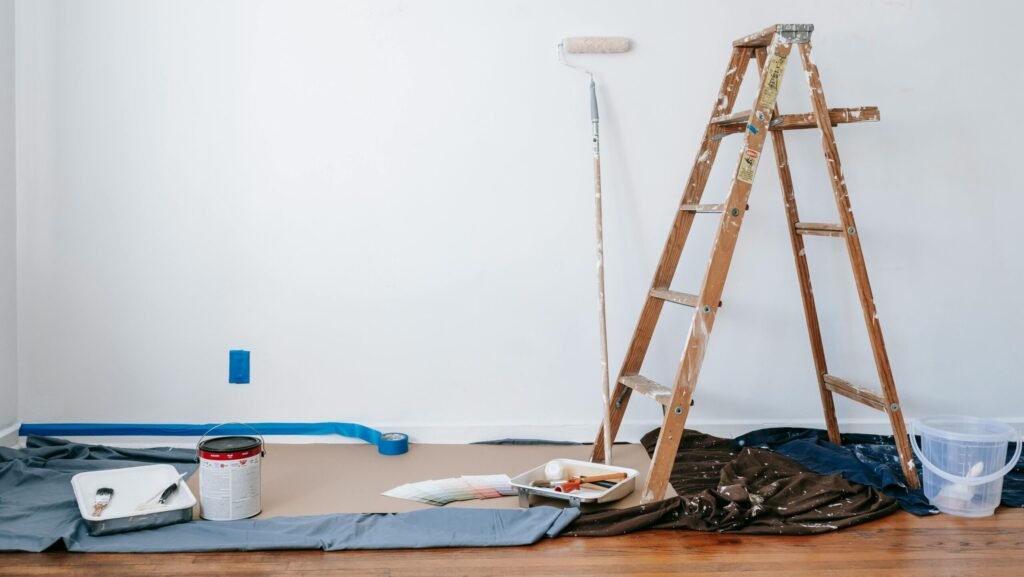 A room prepared for renovation with a ladder, paint supplies, and drop cloth.