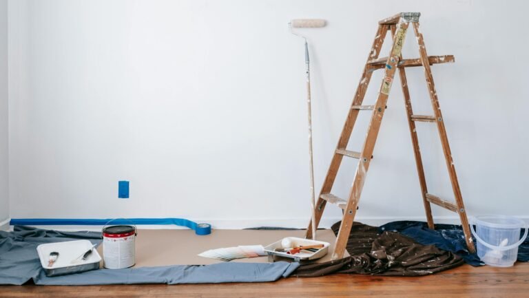 A room prepared for renovation with a ladder, paint supplies, and drop cloth.