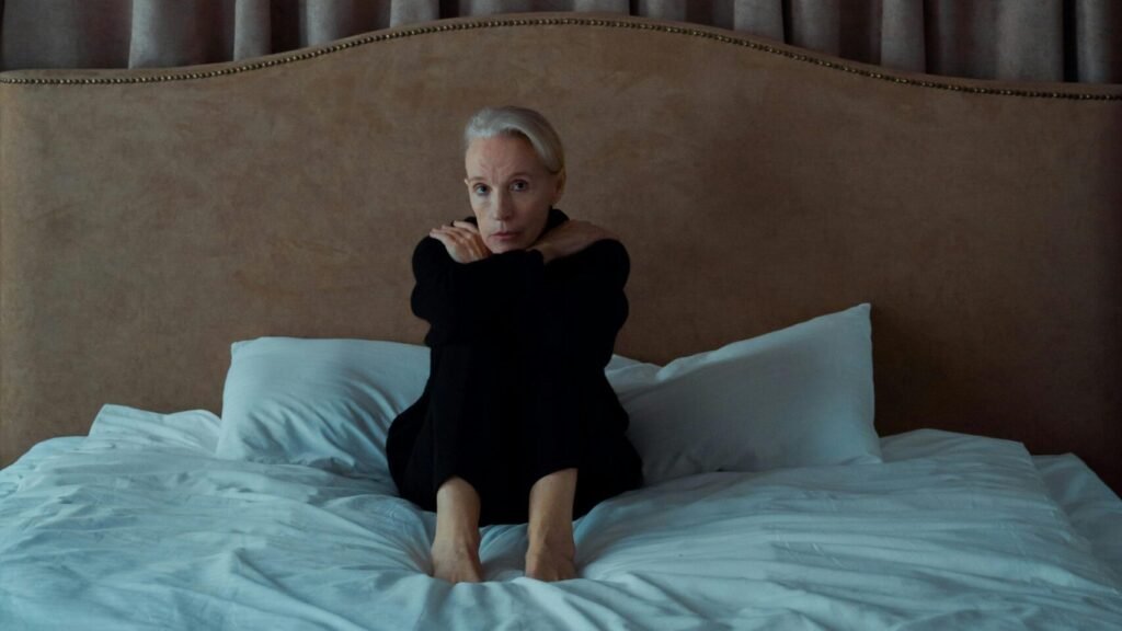A senior woman sits alone on a bed, expressing introspection and melancholy.
