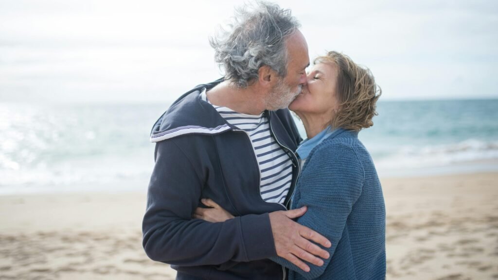 A senior couple shares a romantic kiss on a sunny beach in Portugal, embodying love and companionship.